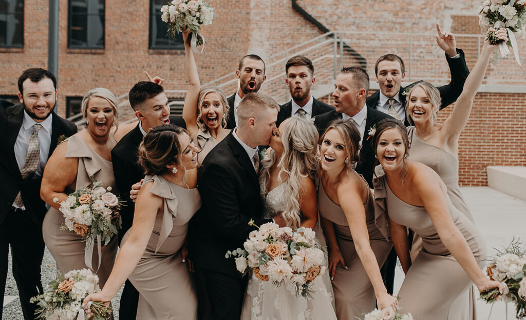 congdon yards courtyard bridal party celebrating while bride and groom kiss