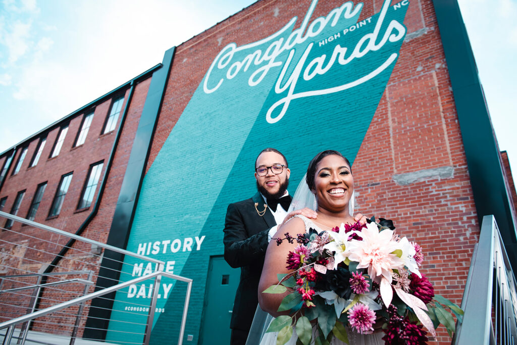 congdon yards courtyard bride and groom smile at camera in front of mural